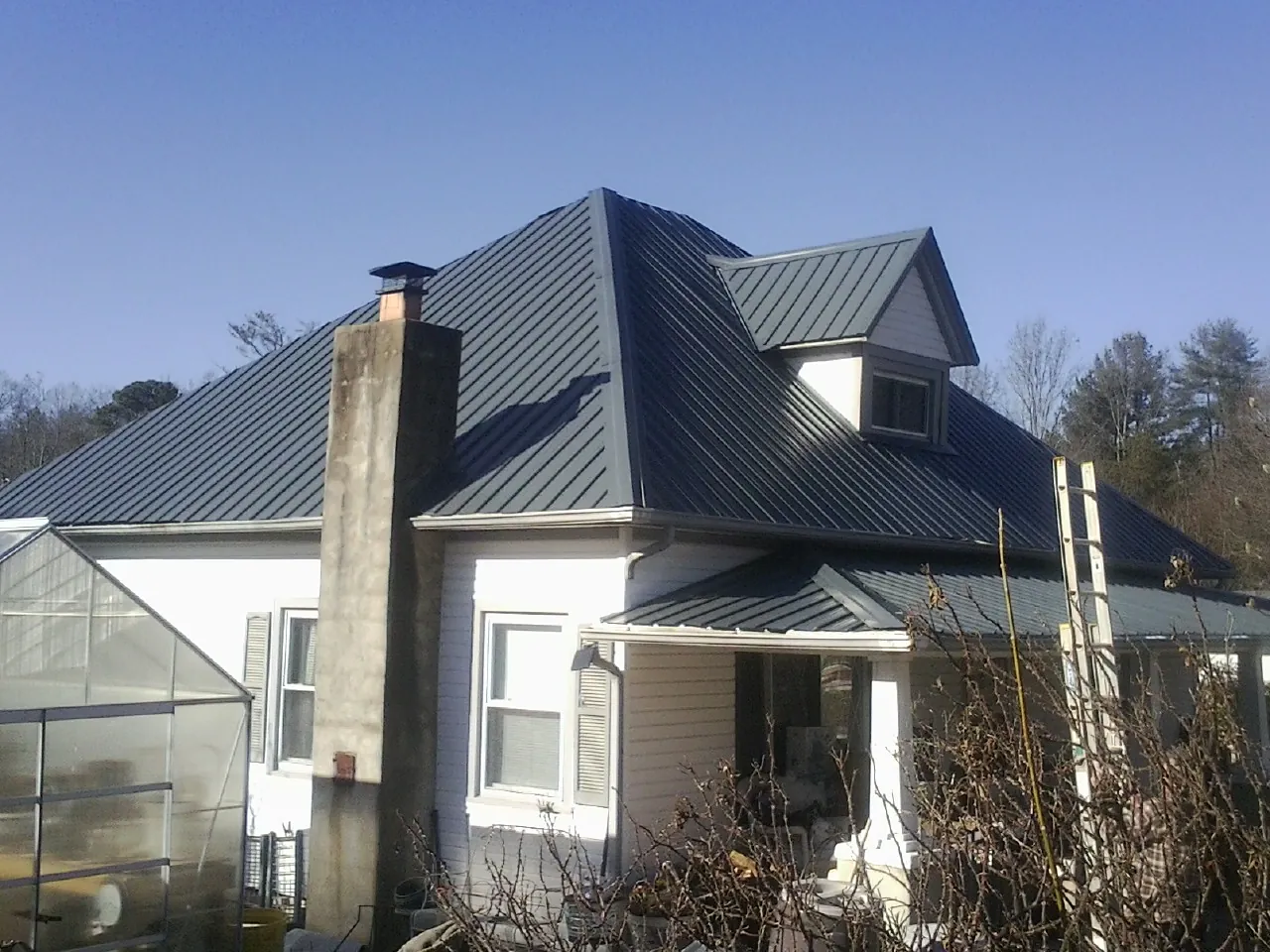 Dark blue standing seam metal roof on a white farmhouse with dormer — Slate & Tile Roof Repair by Roofing Brothers in Rio Linda