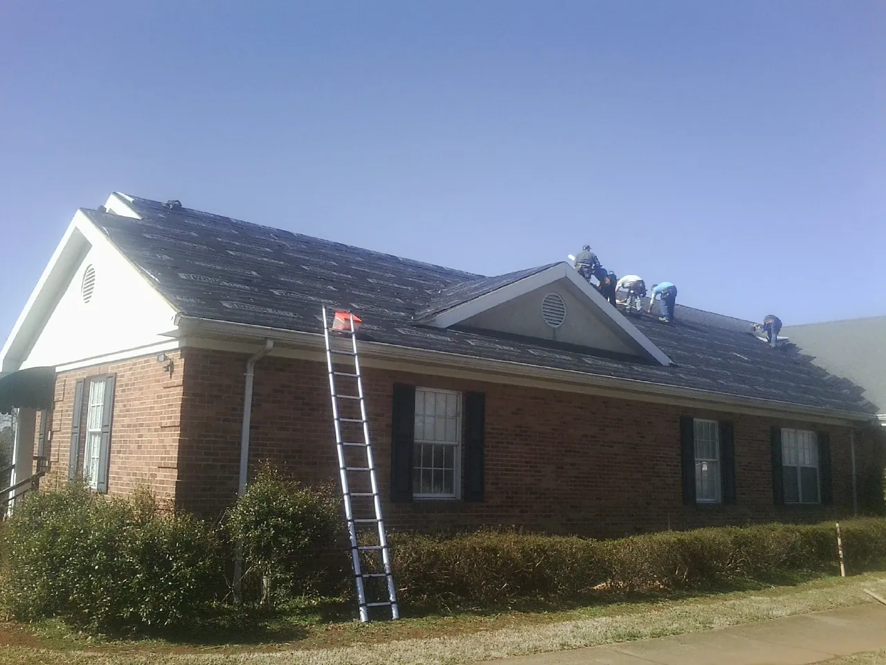 Crew tearing shingles off a brick ranch roof with a ladder set — Emergency Roof Repair work by our crew in Rio Linda