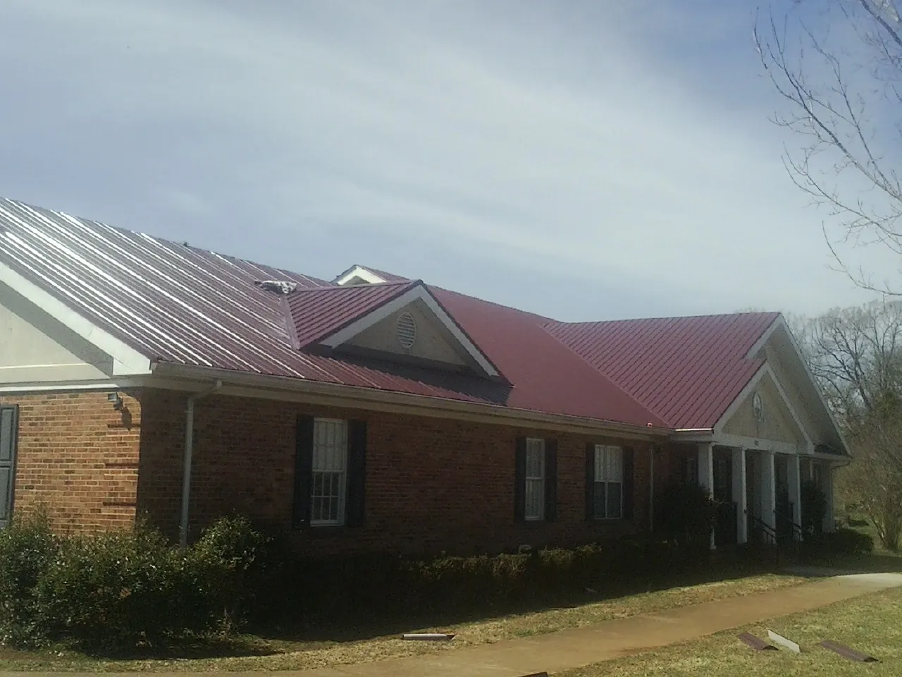 Red metal roof with gabled entries on a long brick building, from a Hail Damage Roof Repair job in Rio Linda