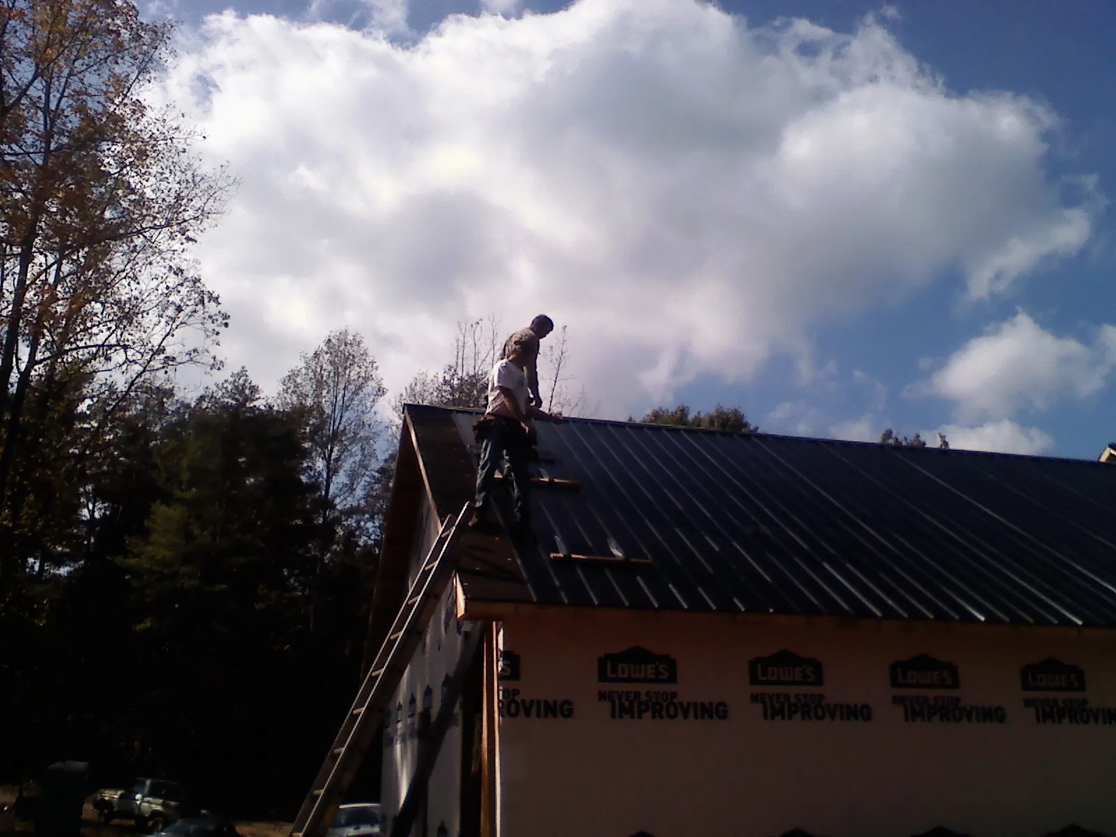 Roofer fastening dark metal panels high against a cloudy sky, from a Roof Inspection job in Rio Linda