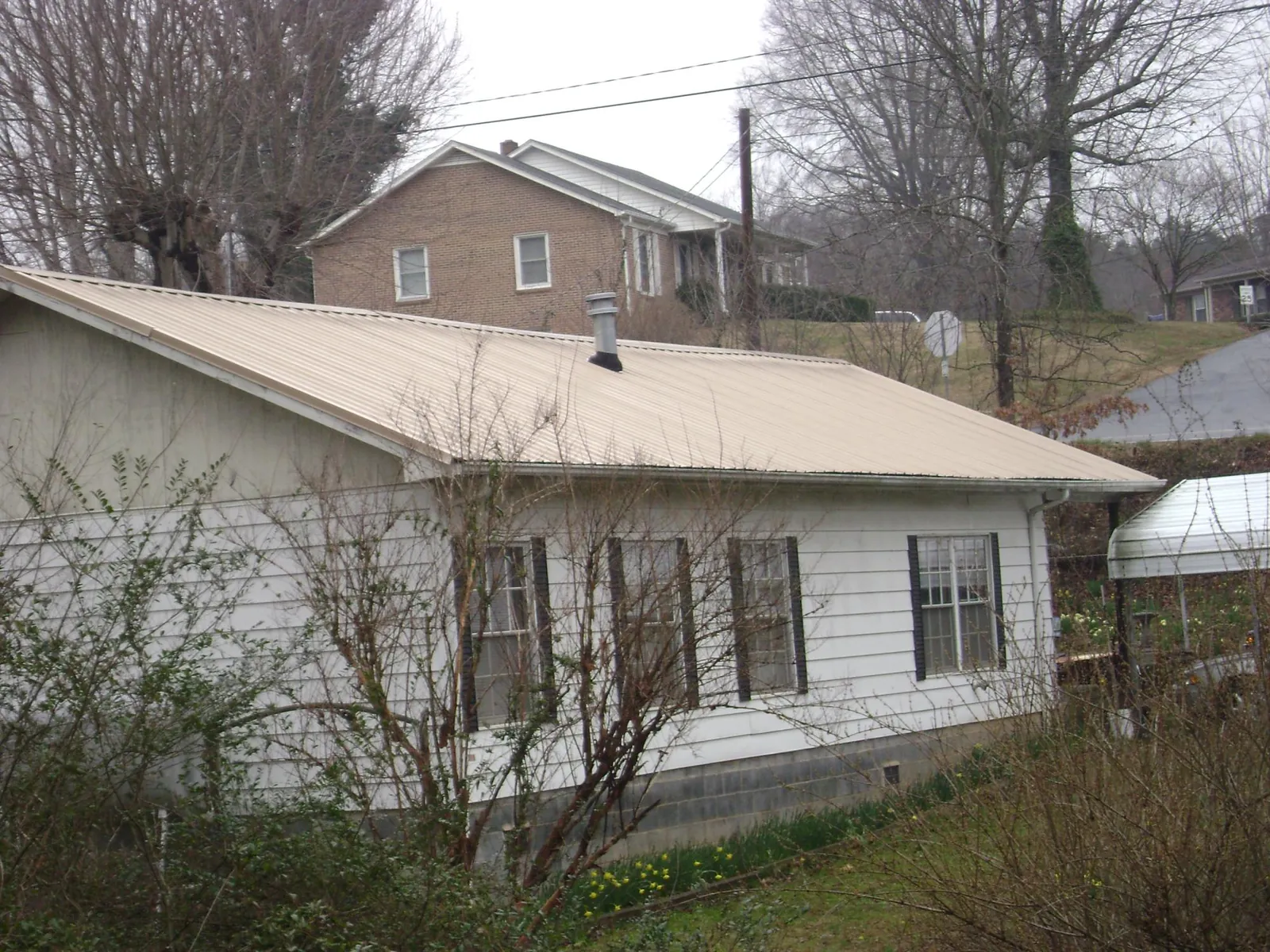 Tan metal roof on a white sided house set into a hillside — Commercial Roofing by Roofing Brothers in Rio Linda